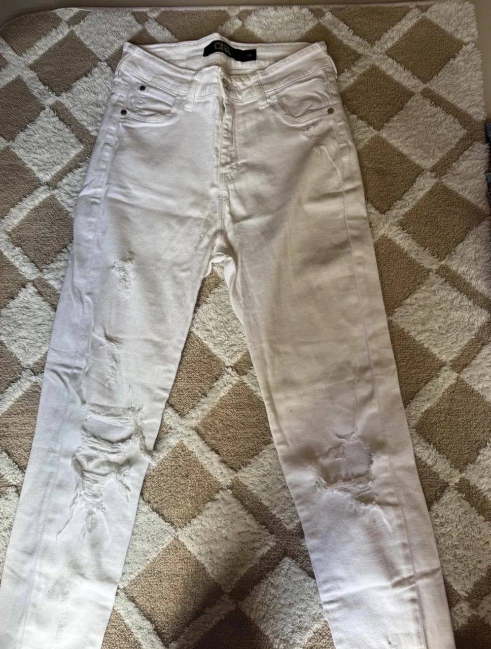 Jeans blancos con roturas en ambas piernas. Cierre y botón en la parte delantera.