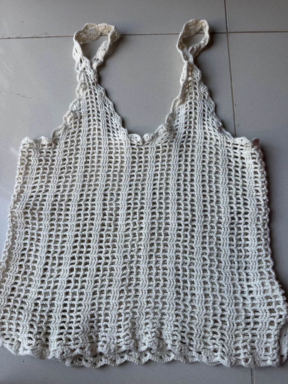 Musculosa tejida a crochet de color crudo. Posee breteles finos y escote en V con borde ondulado. La trama es calada.