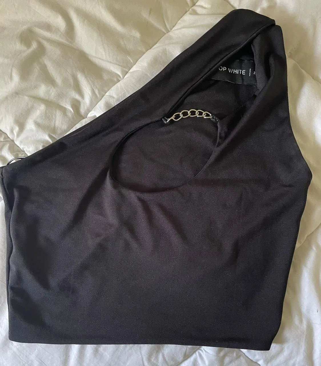 Top negro de un solo hombro con detalle de cadena metálica en el escote.