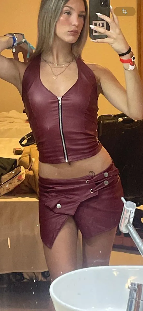 Conjunto de dos piezas color bordó. El top es tipo halter con escote en V y cierre metálico al frente. La falda es corta con detalle de tiras y botones a un costado.