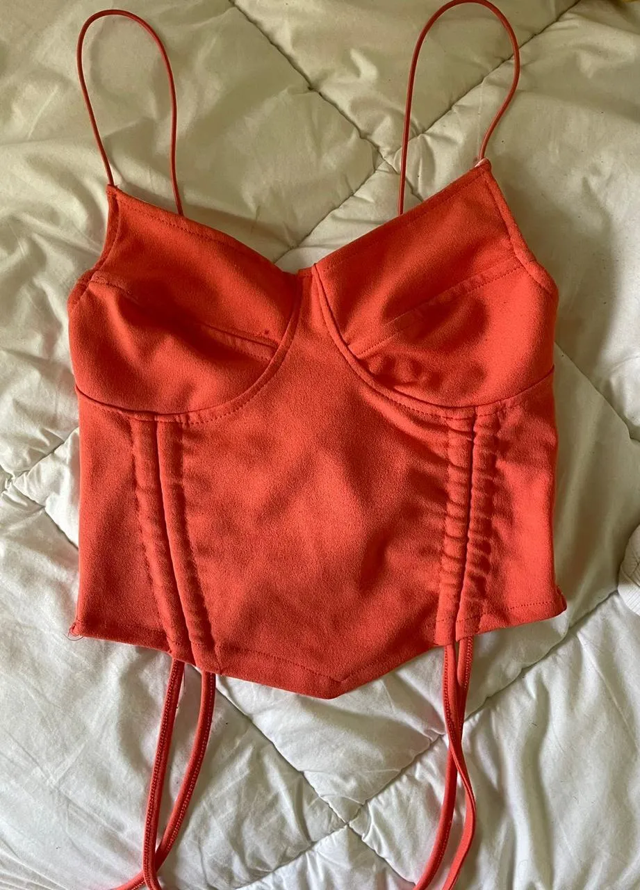 Top de color naranja fluo con tiras finas y detalles de fruncido en los laterales. Posee un diseño tipo corsé con varillas.