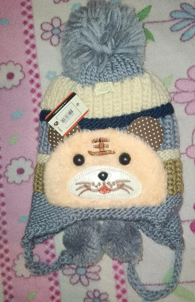 Gorro tejido de lana con diseño de tigre.
Tiene orejas y pompones colgantes. Los colores son variados, con franjas y detalles.