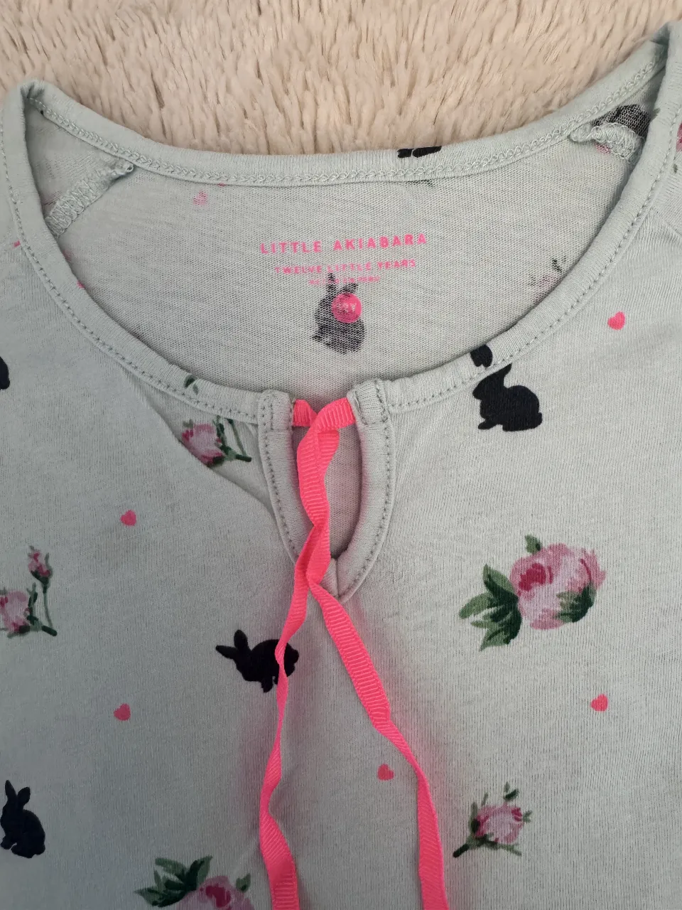 Remera de manga corta para niña, con estampado de conejitos y flores. Tiene un detalle de lazo rosa en el cuello y volados en las mangas. Ideal para un look casual y primaveral. dice talle 12 pero es para un talle 10 