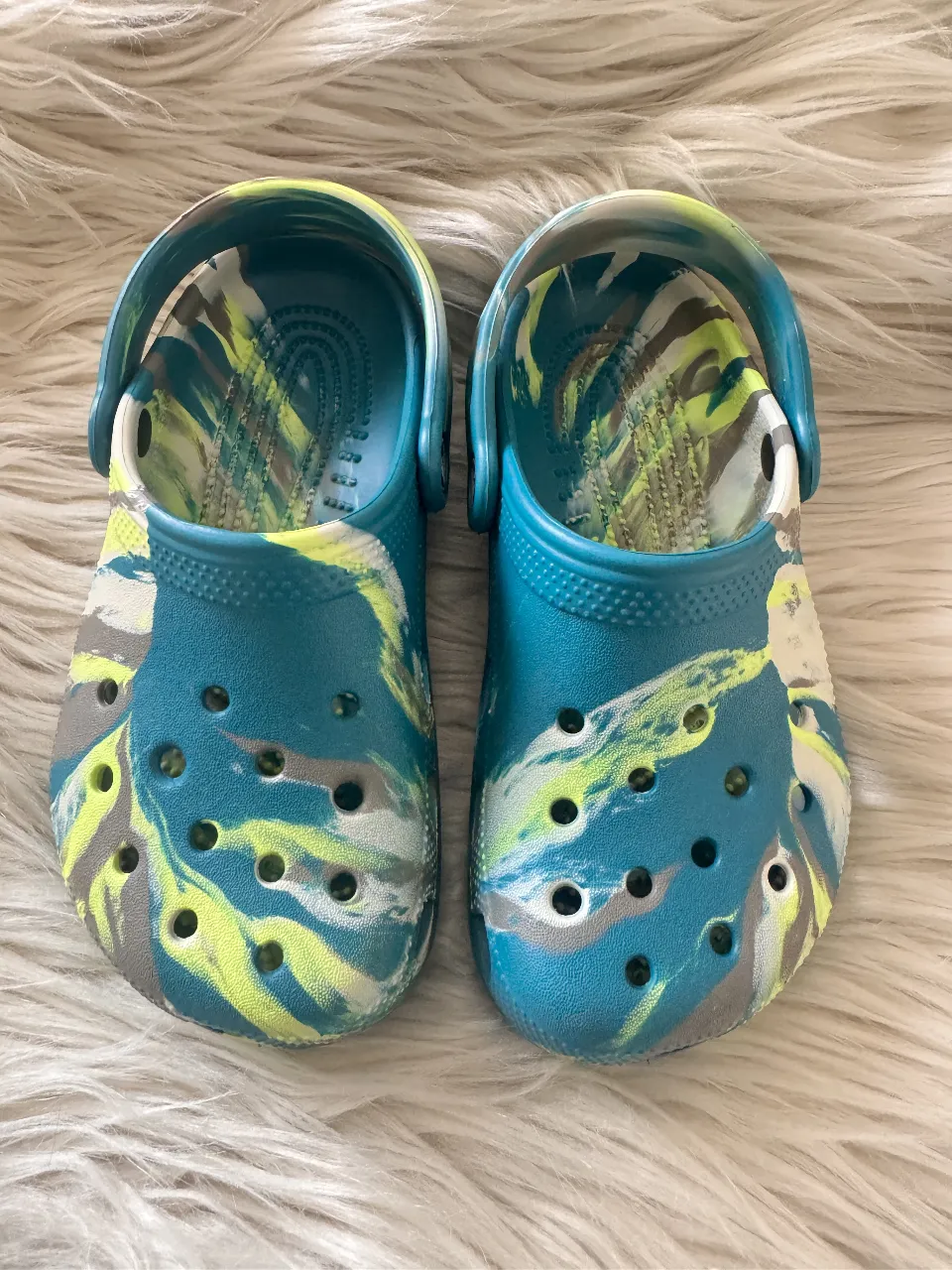 Zuecos Crocs con diseño marmolado en tonos turquesa, amarillo y gris. Ideales para un look casual y cómodo.