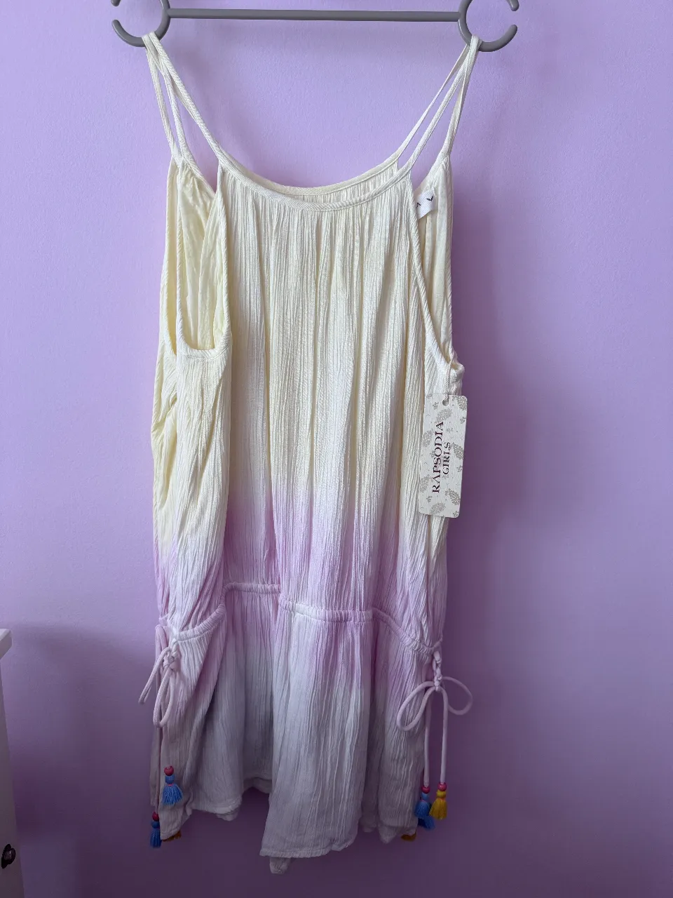 Mono con tirantes finos y detalle de lazos en la parte inferior. Diseño con degradado de color y etiqueta de la marca.