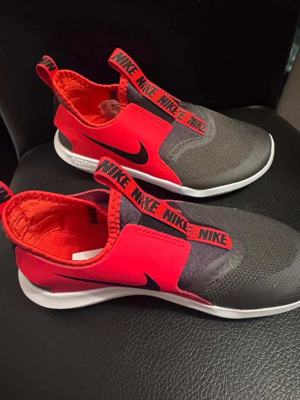Zapatillas Nike Flex Runner para niños, color rojo y gris. Diseño slip-on, ideales para actividades deportivas y uso diario. Con el logo de Nike en la tira y en el lateral.
