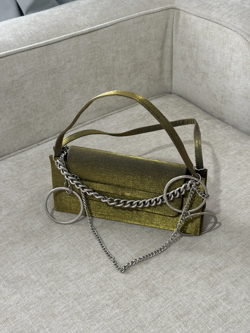 Cartera de mano dorada con cadena plateada y detalles de aros. Ideal para eventos y fiestas.