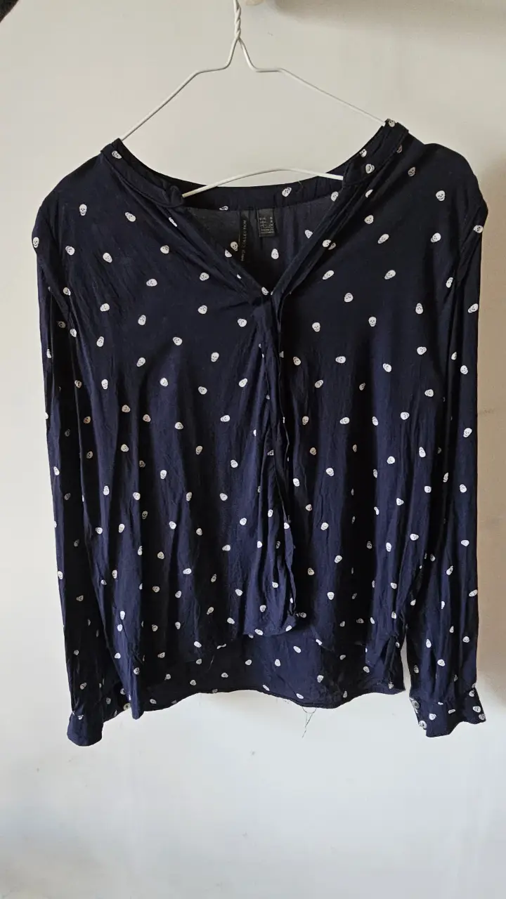 Blusa de manga larga azul marino con estampado de calaveras blancas. Cuello en V y detalle de lazo. Ideal para un look casual y moderno.