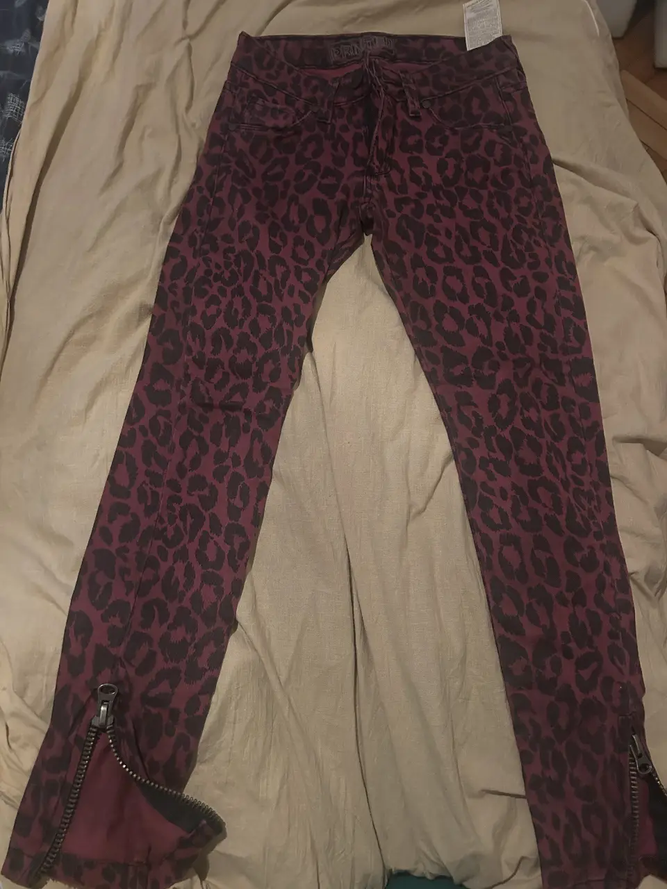 Jeans de mujer con estampado de leopardo en tonos borgoña y negro. Diseño de tiro medio, corte recto y detalles de cierre en los tobillos. Ideal para un look audaz y moderno.