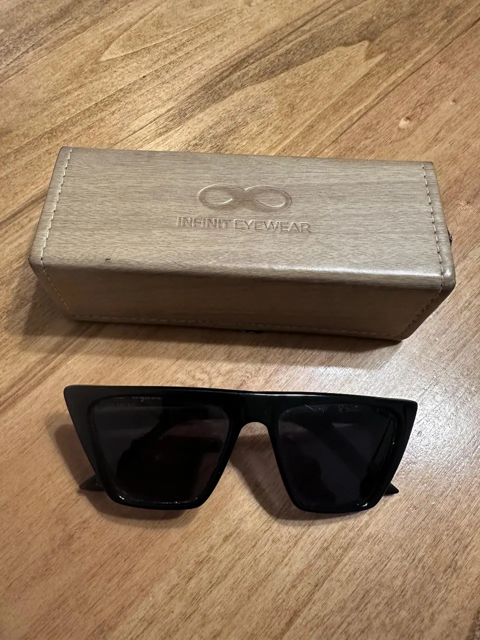 Anteojos de sol negros con marco cuadrado y estuche de madera. Diseño moderno y elegante, ideales para proteger tus ojos con estilo.
