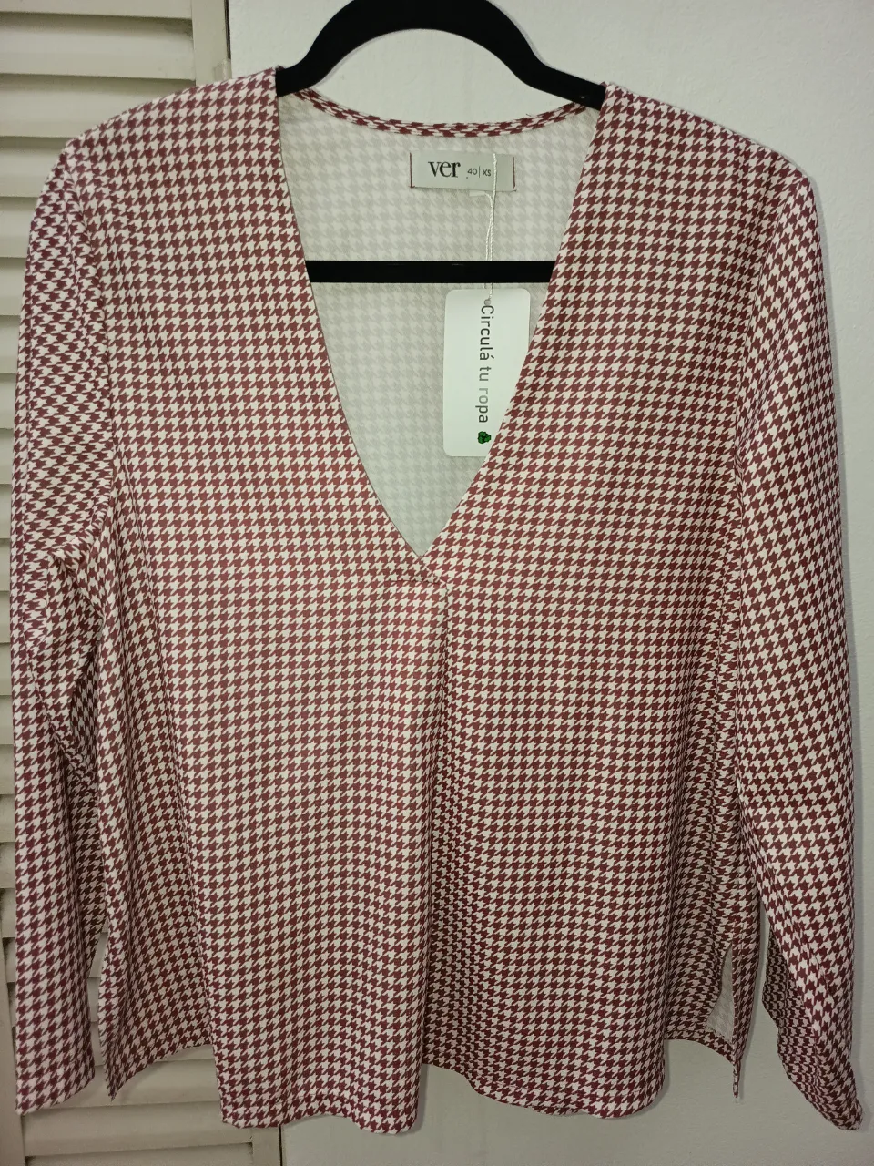 Blusa estampada con cuello en V y mangas largas. Presenta un patrón de cuadros pequeños en tonos tierra y blanco.