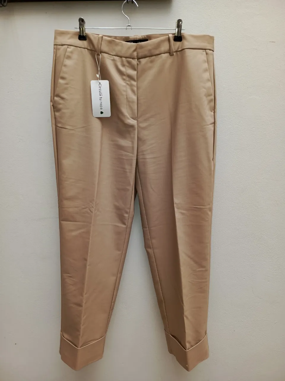 Pantalón color beige, con bolsillos laterales y puños anchos en los tobillos. Cierre y botón en la parte frontal.