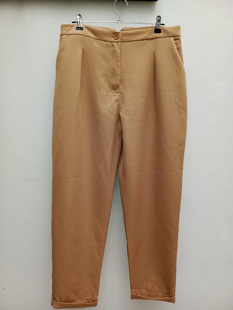 Pantalón color marrón claro, con pinzas en la parte delantera y un botón en la cintura.