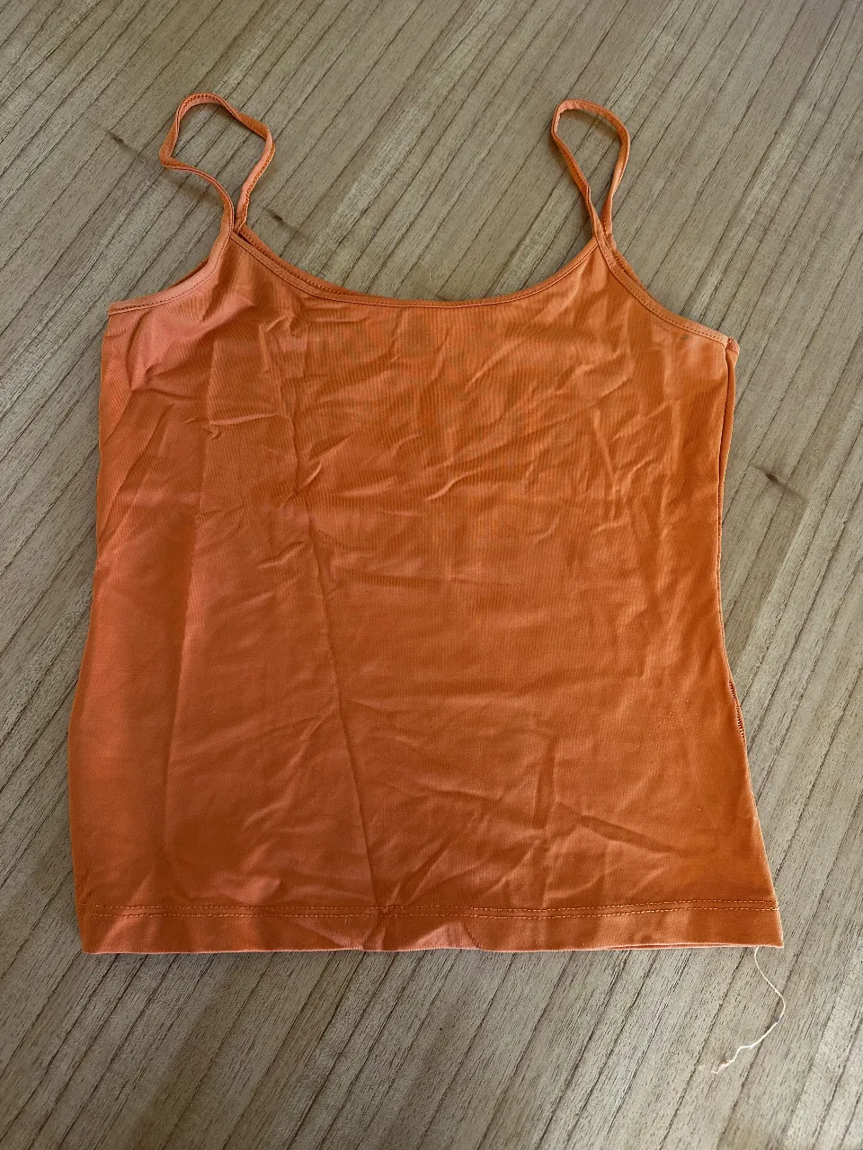 Top musculosa naranja con breteles finos, ideal para el verano. Perfecto para combinar con jeans o shorts.