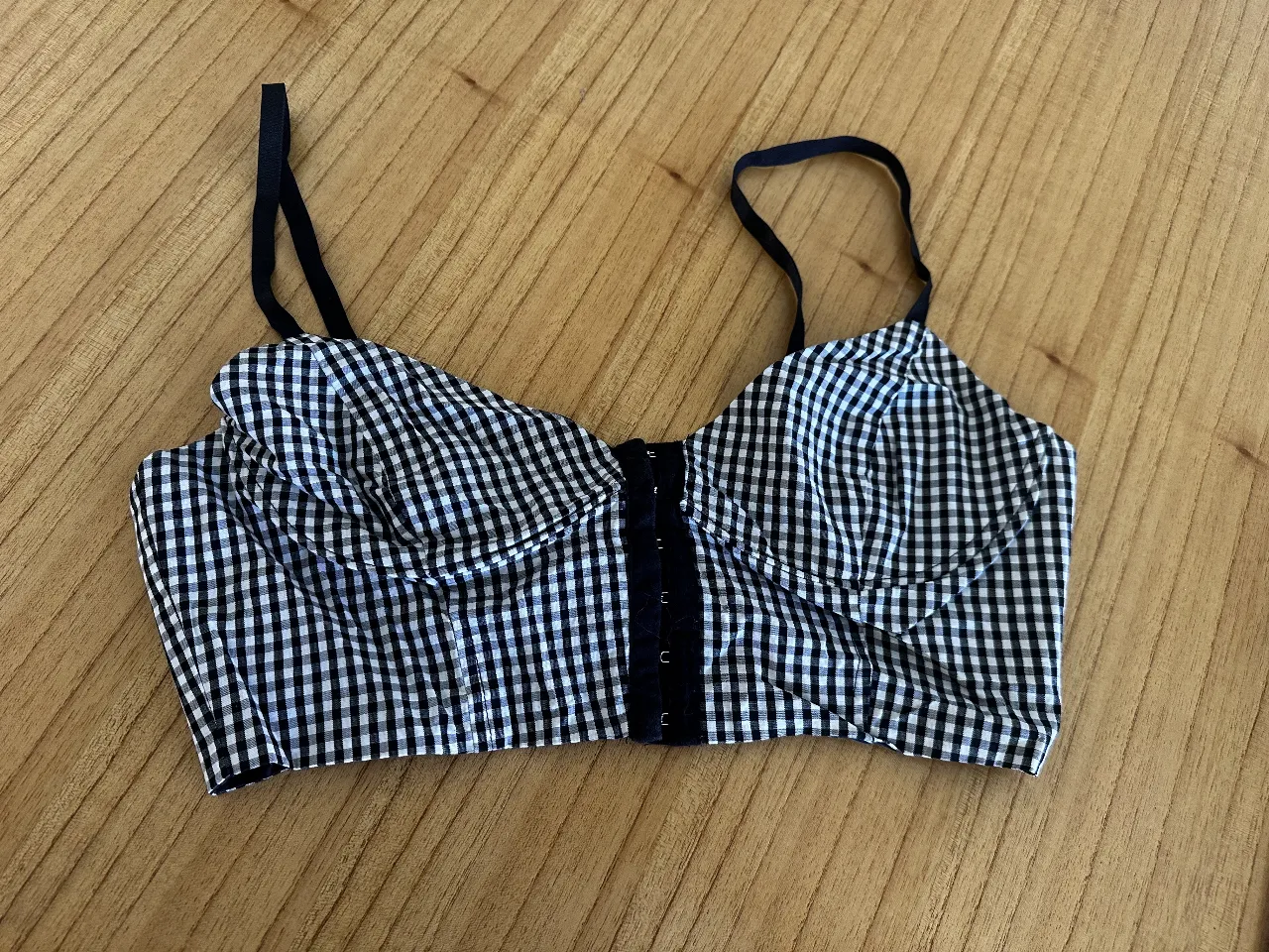 Top corset con estampado de cuadros vichy en blanco y negro. Diseño con ballenas y cierre frontal. Ideal para un look moderno y femenino.