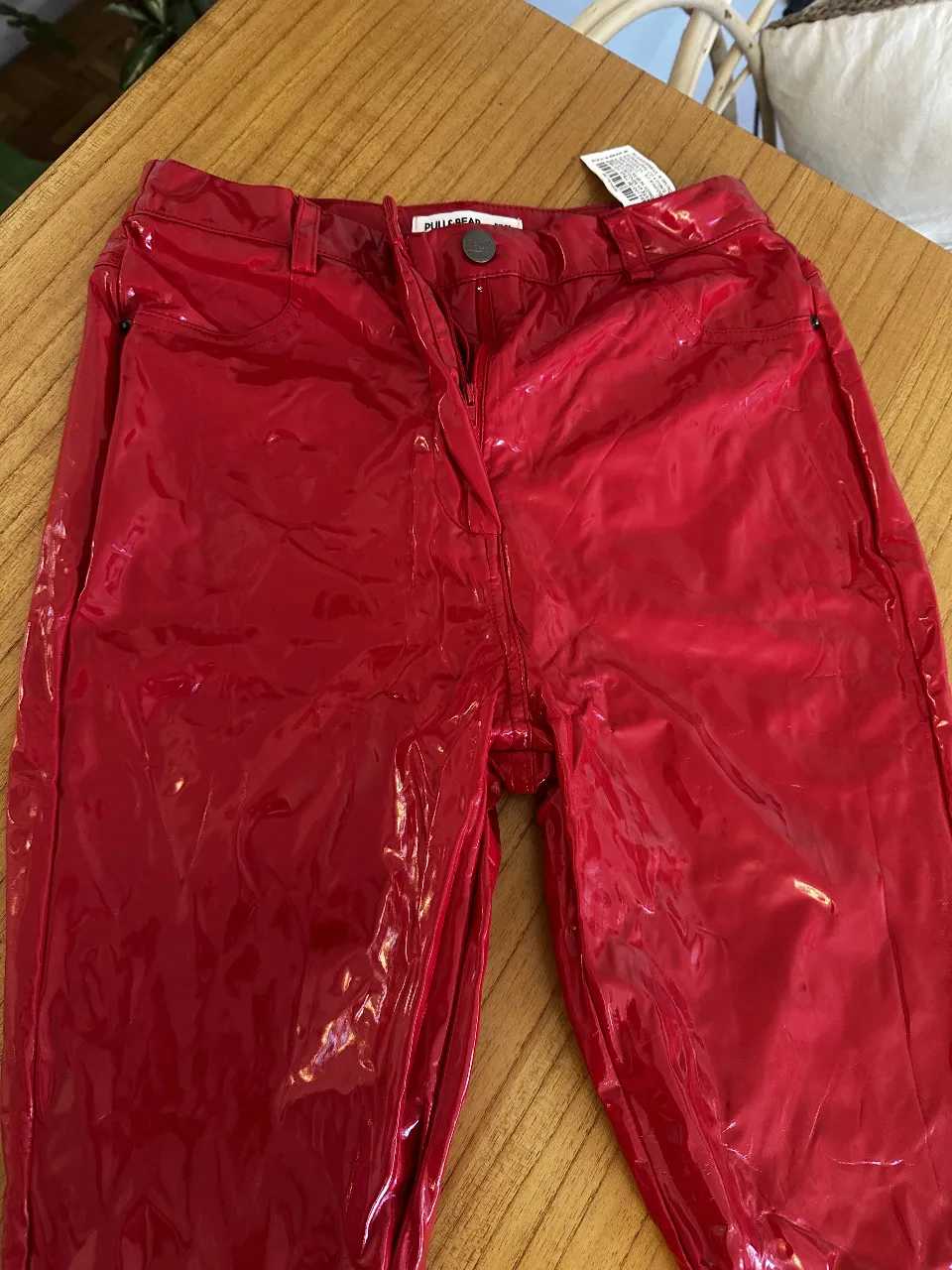 Pantalón de vestir rojo engomado con un acabado tipo charol. Tiro medio, con bolsillos traseros y cierre frontal. Ideal para un look audaz y moderno. comprado en Barcelona en Pull & Bear 