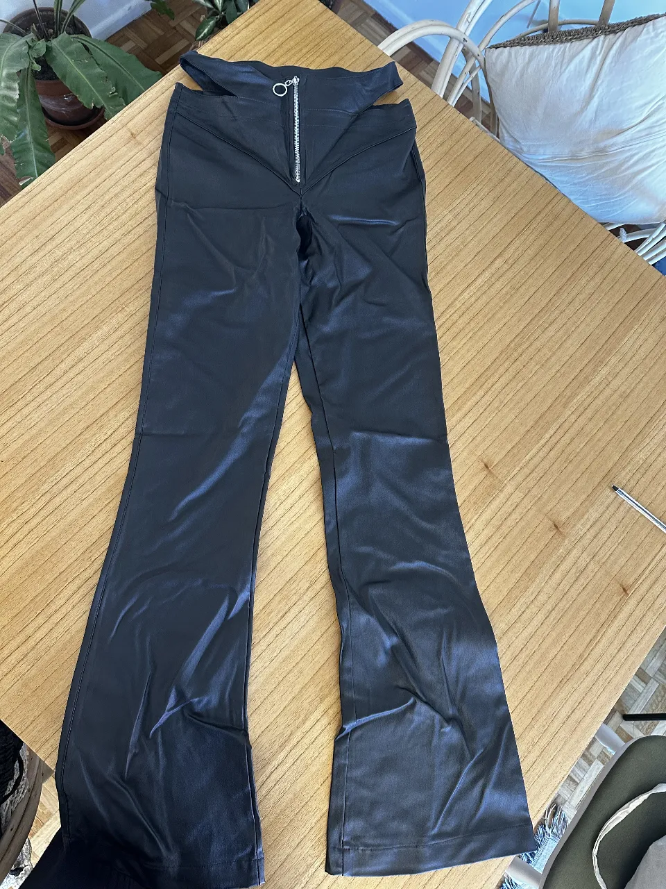 Pantalón de mujer negro tipo flare, Simil cuero con diseño cut out en la cintura y cierre frontal. Estilo moderno y audaz, ideal para looks de fiesta o salidas.