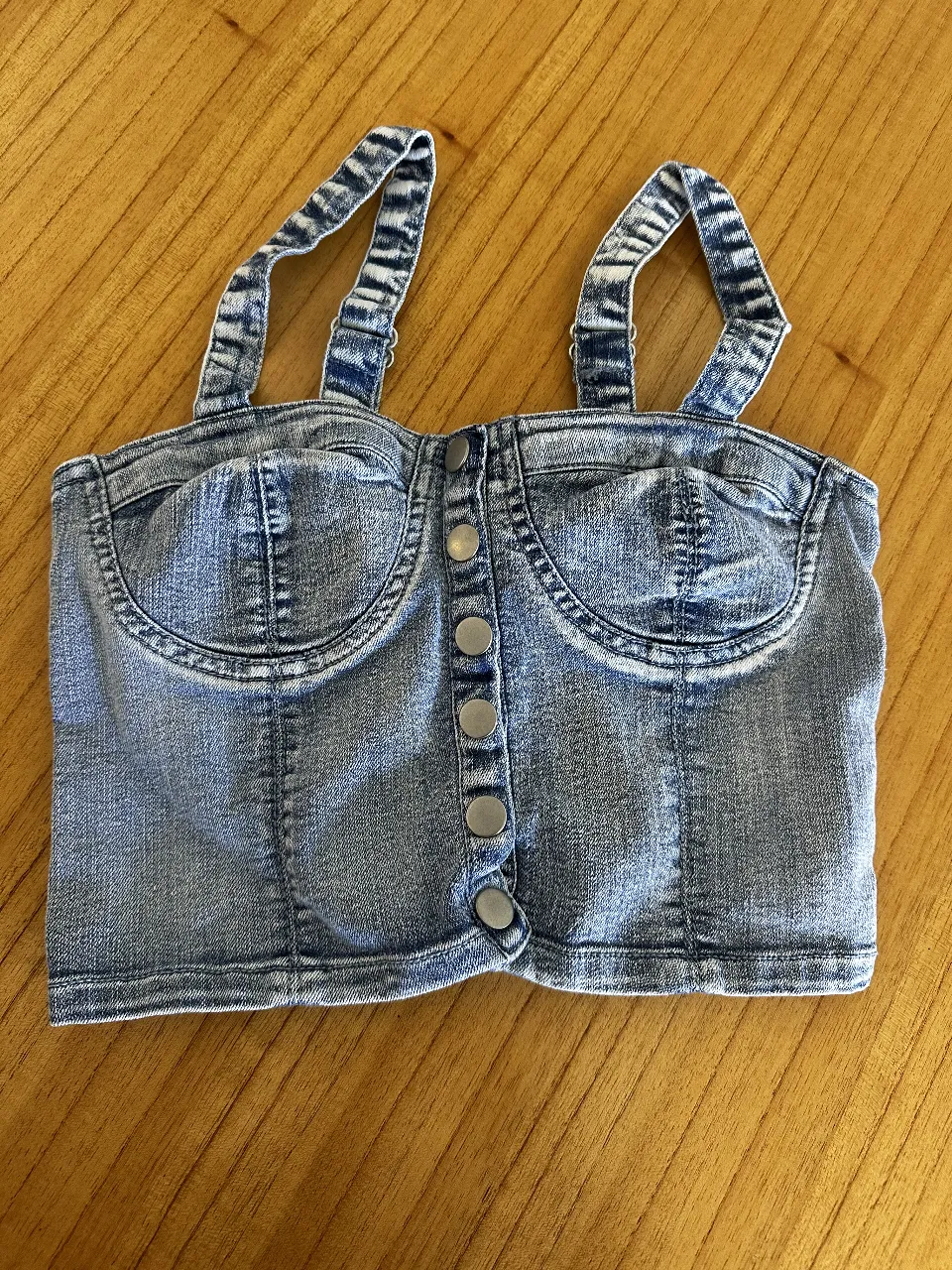Top de jean con tiras y botones frontales. Estilo moderno y versátil, ideal para combinar con diferentes outfits.