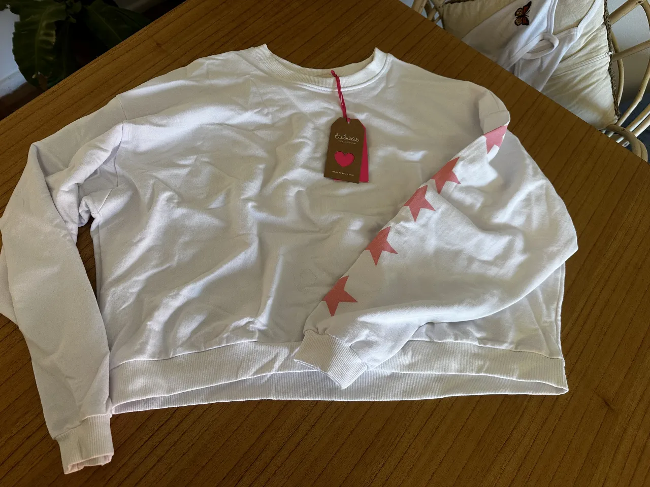 i Buzo cortito de cuello redondo blanco con mangas largas y detalle de estrellas rosas en una manga. Ideal para un look casual y cómodo.