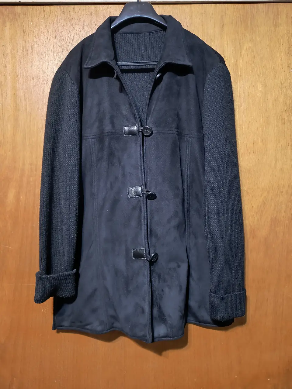 Tapado negro con mangas de tejido de punto y cierre con botones. Ideal para el invierno, combina estilo y abrigo.