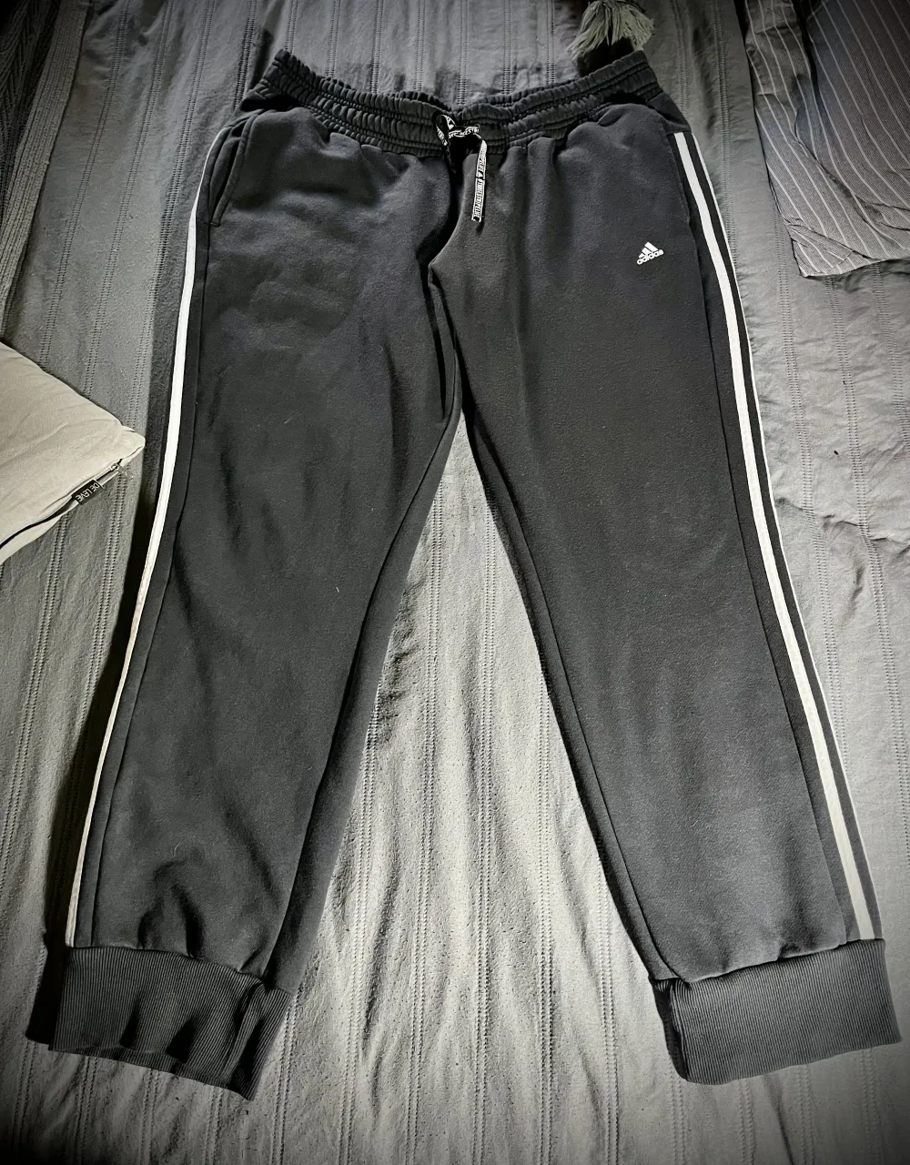 Pantalón de algodón gris plomo 🩶 con las tres tiras blancas a los costados y logo de Adidas bordado. Cintura elastizada con cordón. Terminación de ribb en puños anchos.. Bolsillos delanteros. 
Calce holgado.  Está en muy buen estado, salvo minimo desgaste por del uso, que fue en pocas ocasiones. 