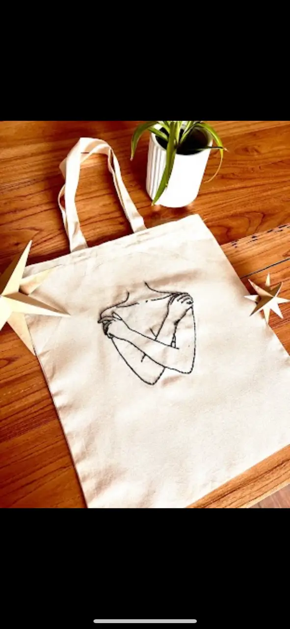 Bolso tote de tela cruda con diseño de bordado de figura humana abrazándose. Ideal para llevar tus cosas con estilo y un toque artístico.