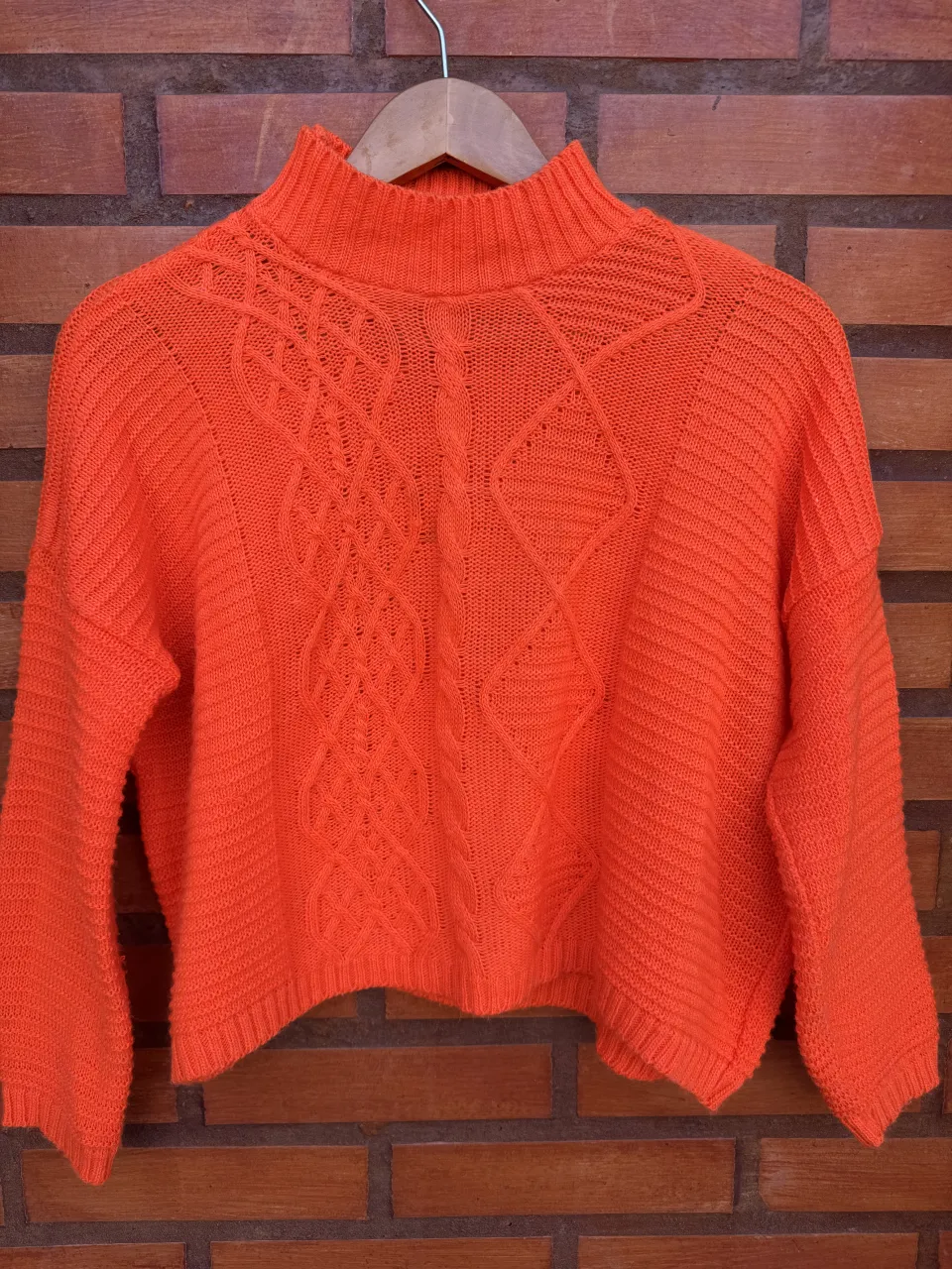 Sweater naranja de cuello alto con detalles tejidos en el frente. Manga larga y corte crop. Ideal para un look canchero y abrigado.