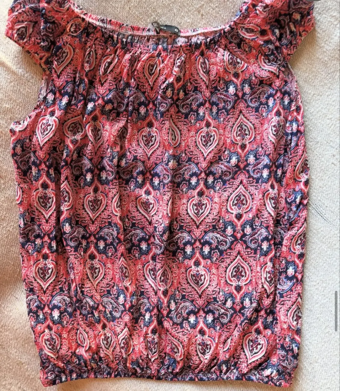 Blusa estampada con diseño paisley en tonos rojos y azules. Corte holgado con elástico en la cintura y mangas cortas. Ideal para un look casual y fresco.