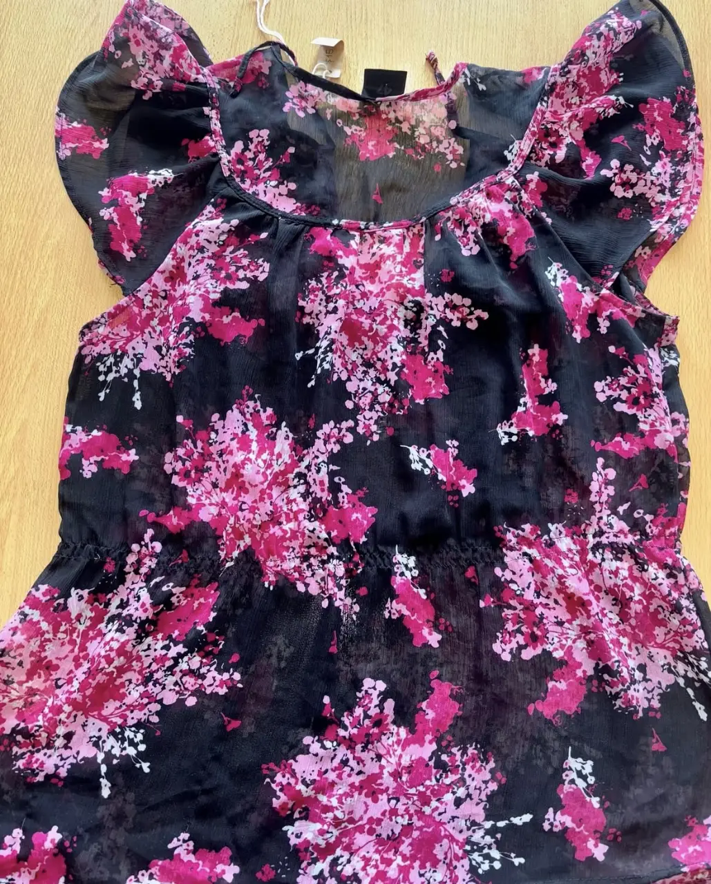 Blusa de mujer con estampado floral en tonos rosa y negro. Diseño con mangas cortas tipo volantes y detalle elástico en la cintura. Ideal para un look fresco y femenino.