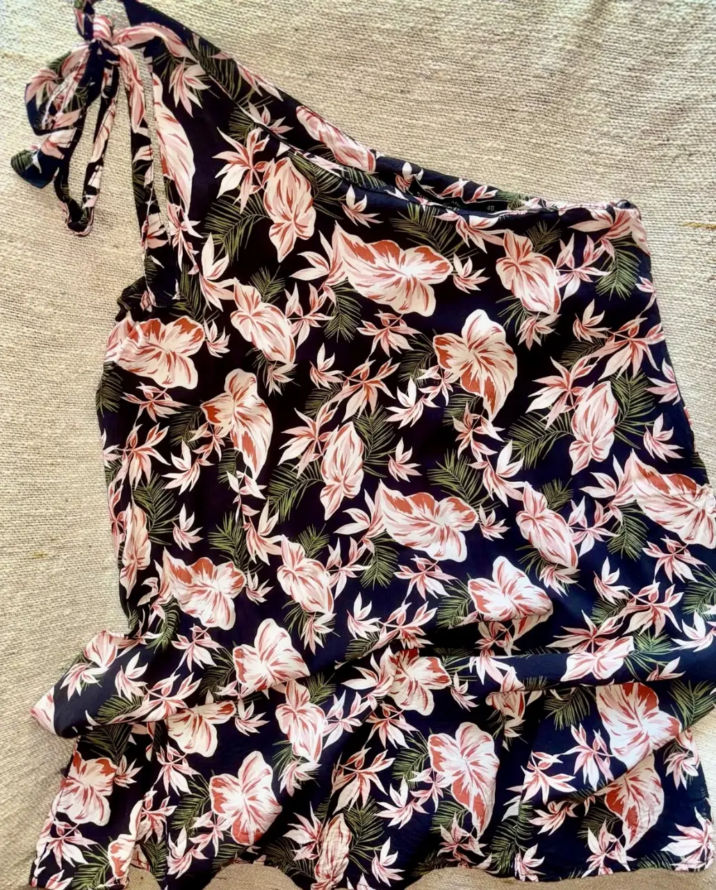 Vestido mini con estampado floral en tonos rosa y blanco sobre fondo negro. Diseño asimétrico con un solo hombro y detalle de lazo en la tira. Ideal para un look fresco y moderno.