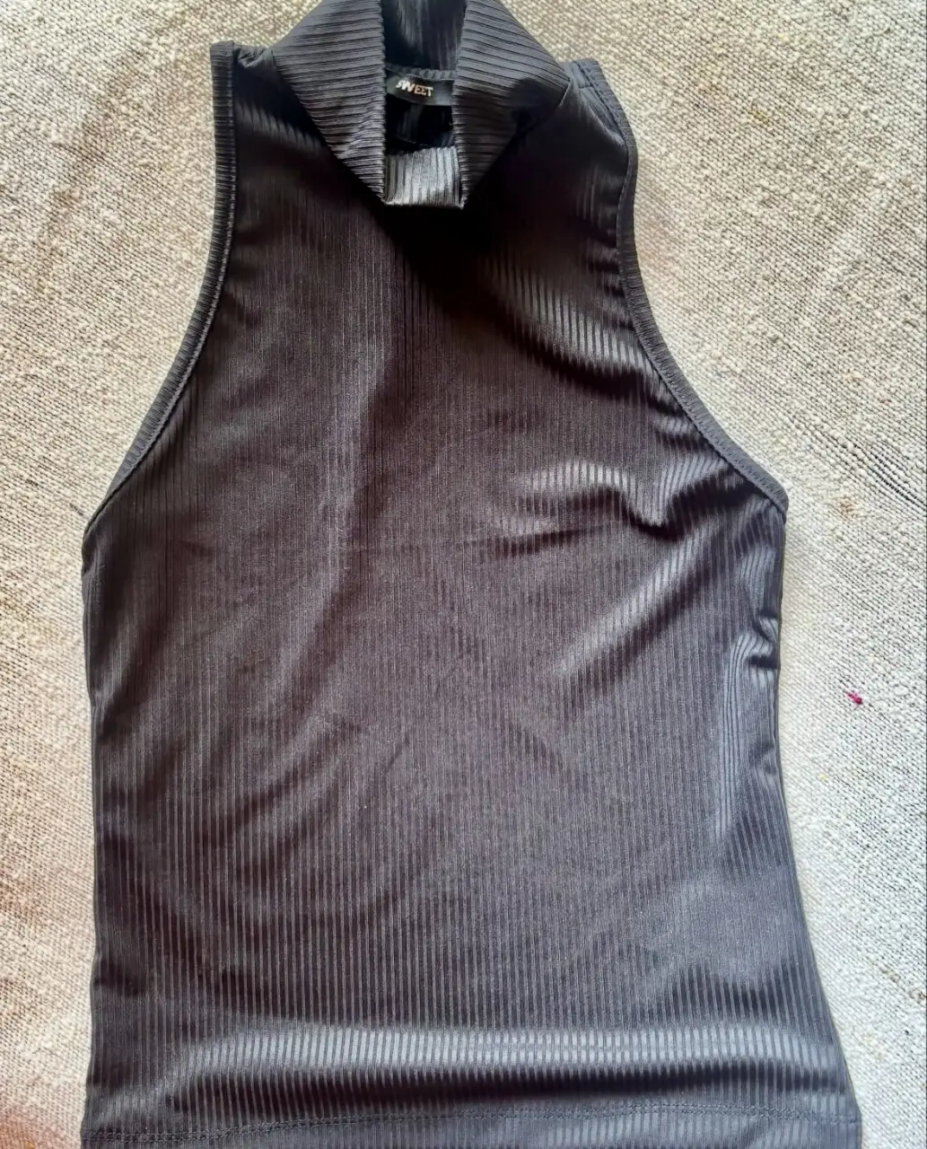Top negro de cuello alto y sin mangas, ideal para un look moderno y versátil. Confeccionado en tela acanalada, este top es perfecto para combinar con jeans, faldas o pantalones de vestir. La etiqueta dice SWEET.