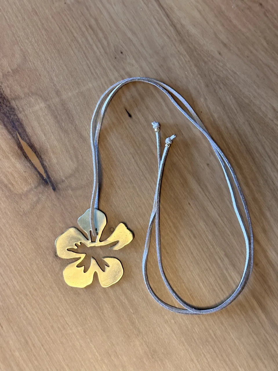 Collar acero quirúrgico bañado en oro con dije de flor dorada y cordón de cuero color topo. Ideal para la playa o el verano. 