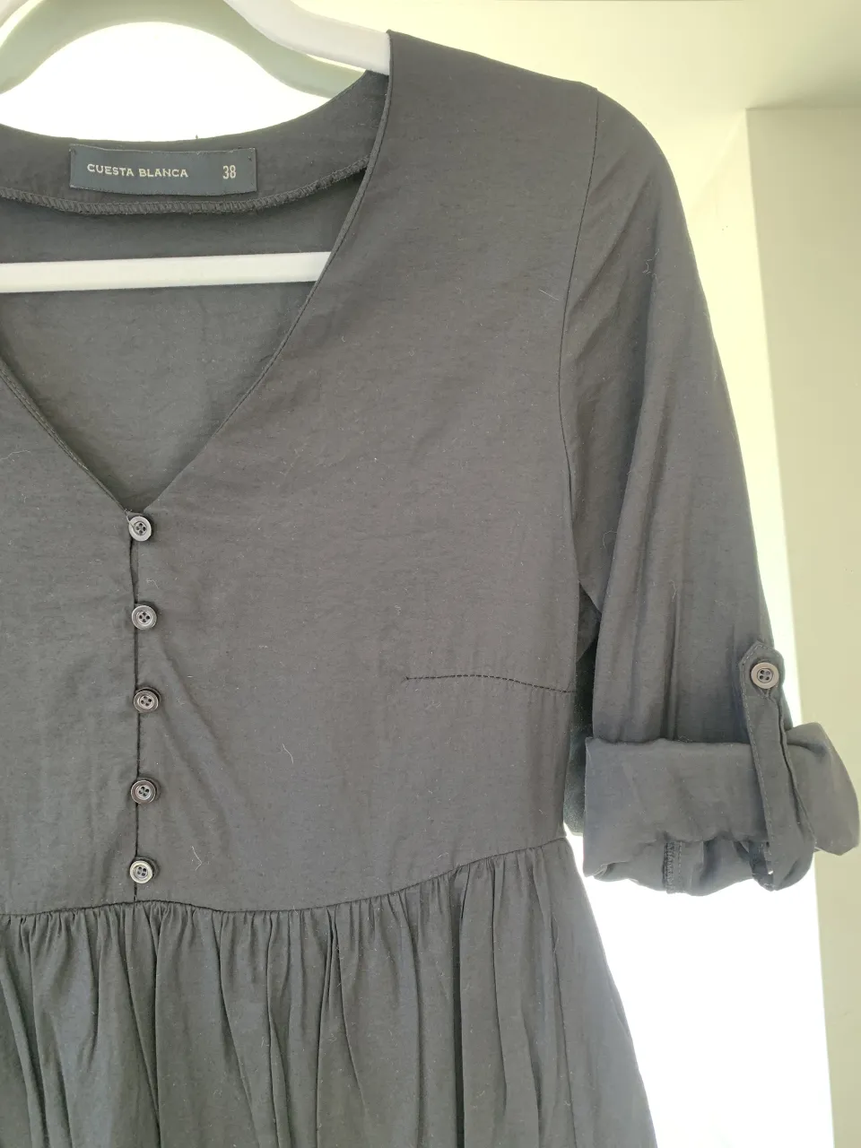 Vestido negro de taffeta Cuesta Blanca talle S con cuello en V, botones al frente y mangas largas con boton para arremangar. Posee volados en la parte inferior. Altura arriba de la rodilla. Dos usos, sin detalles