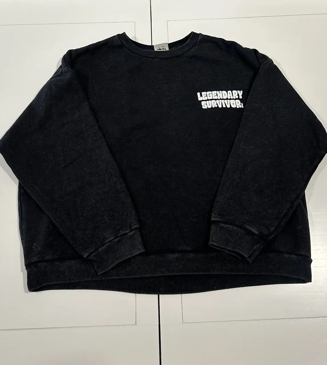 Buzo de cuello redondo negro con estampado "Legendary Survivor" en blanco en la parte delantera y un diseño de calaveras amarillas y rosas violetas en la espalda. Estilo streetwear y vintage.