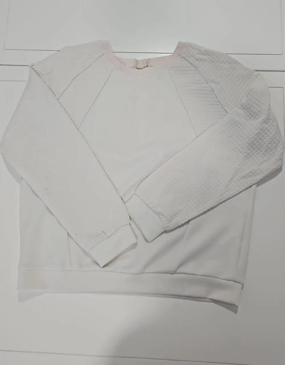 Buzo de cuello redondo blanco, con mangas en tela texturizada. 