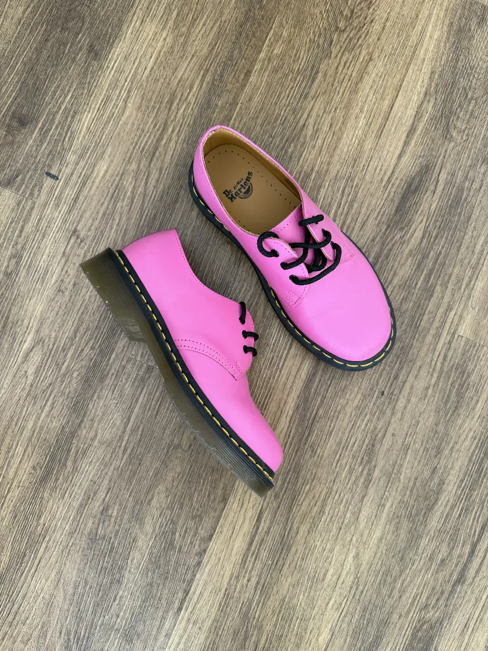 Zapatos Dr. Martens color rosa, con cordones negros y suela negra con costuras amarillas. Un clásico renovado para un look moderno y audaz.