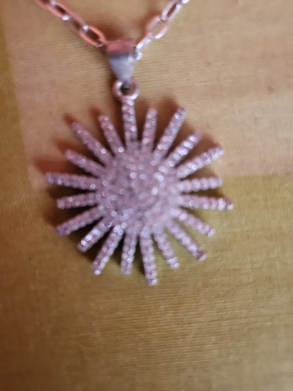 Collar plateado con dije en forma de sol con piedras brillantes.