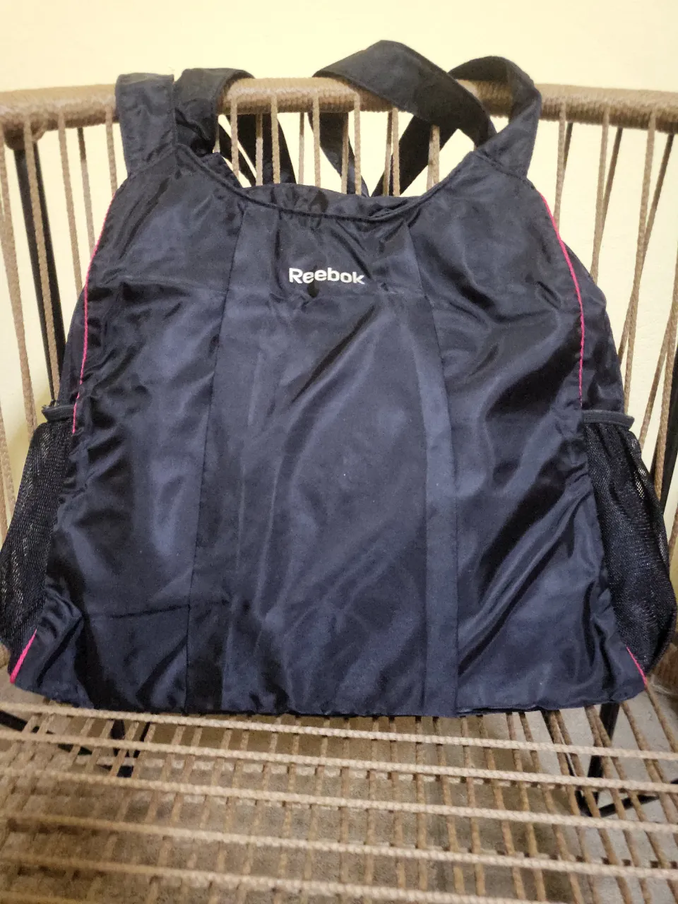 Bolso deportivo negro de la marca Reebok, ideal para llevar tus pertenencias al gimnasio o para el día a día. Cuenta con bolsillos laterales de red y detalles en color rosa que le dan un toque moderno. Su diseño es práctico y funcional.