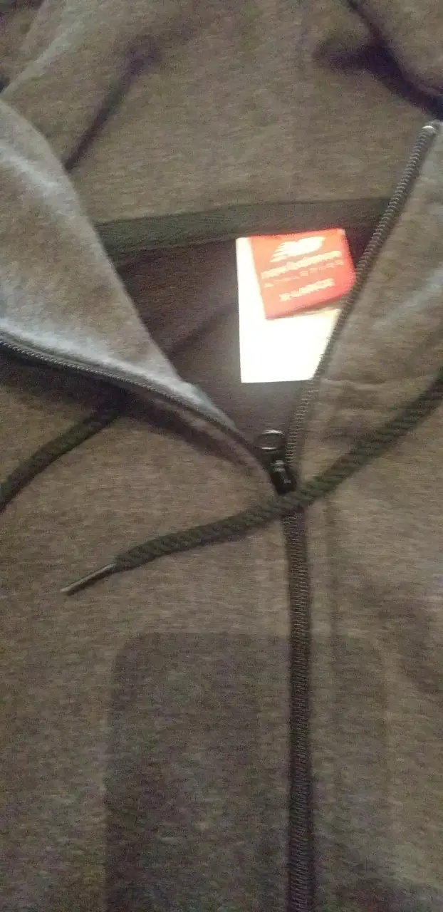 Buzo con cierre New Balance para hombre, color gris, con capucha y bolsillo tipo canguro. Ideal para un look casual y deportivo.