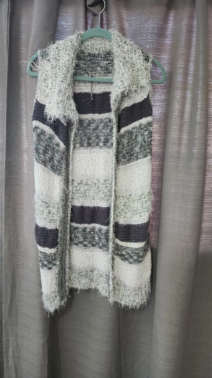 Chaleco tejido a rayas en tonos de gris, blanco y negro. Posee cuello solapa y terminaciones desflecadas.