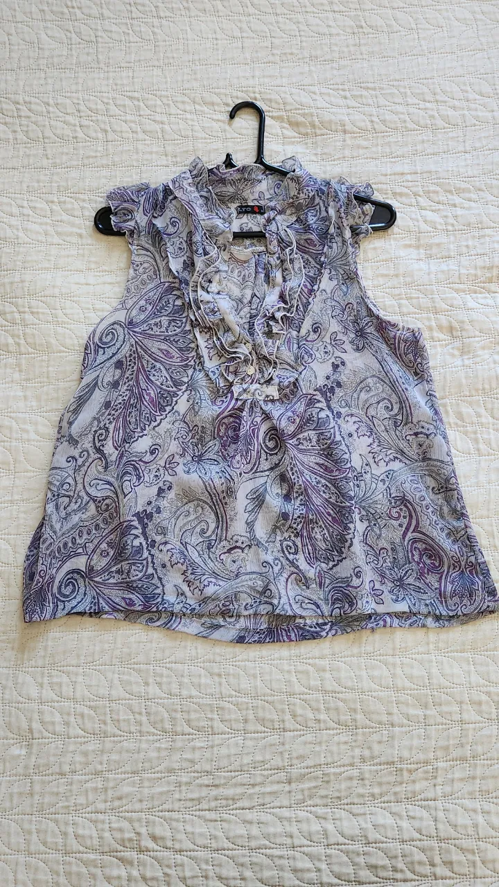 Blusa sin mangas con cuello mao y volados en el cuello y mangas. Estampado floral y paisley en tonos lilas, grises y blancos.