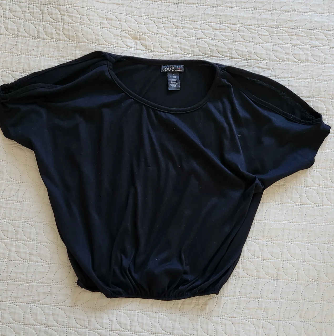 Remera negra con mangas cortas y escote redondo. Posee un detalle de fruncido en la cintura.