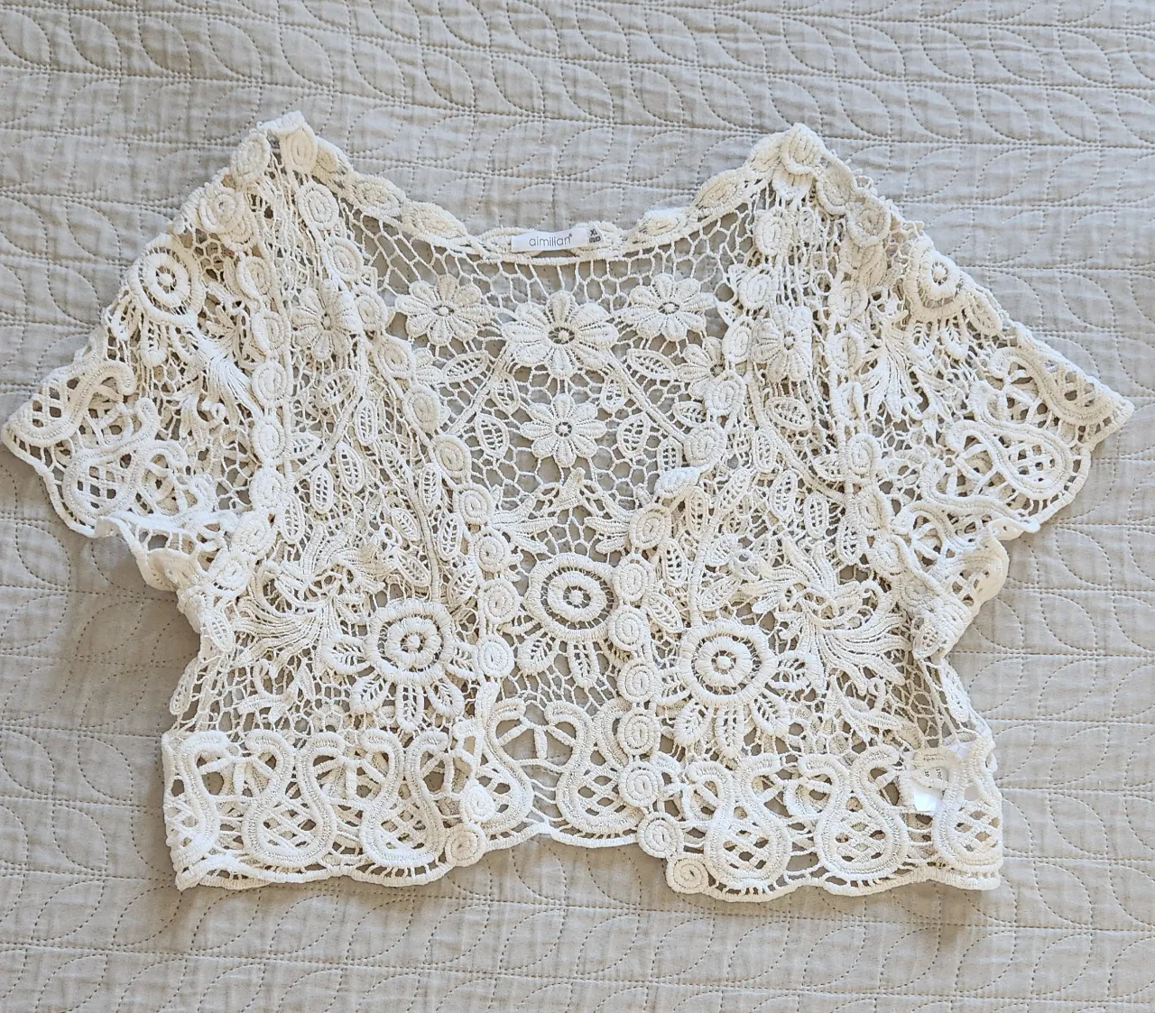 Top de crochet blanco con mangas cortas y detalles florales.