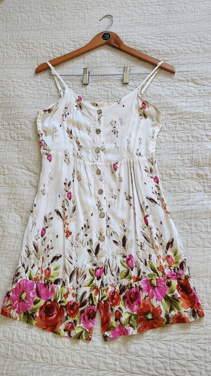 Vestido blanco con estampado floral en tonos rosas, rojos y verdes. Posee breteles finos y botones en la parte delantera.