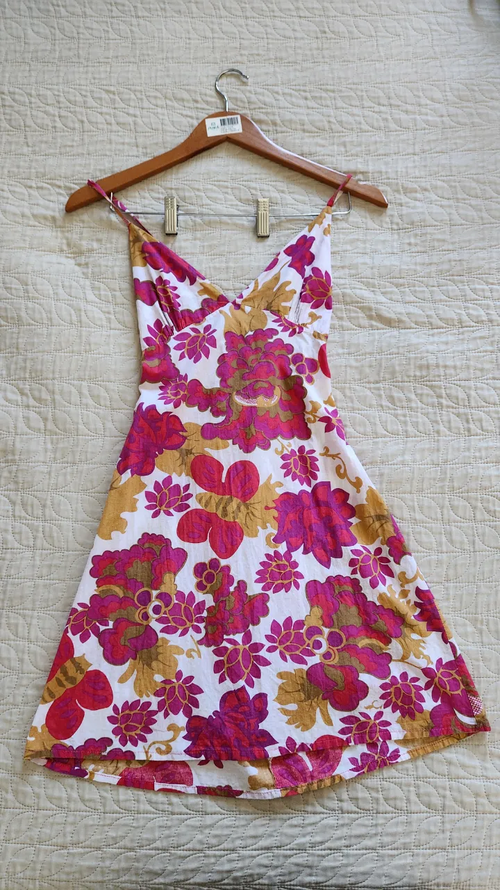 Vestido corto con estampado floral en tonos fucsia, dorado y blanco. Breteles finos y espalda con tiras cruzadas.