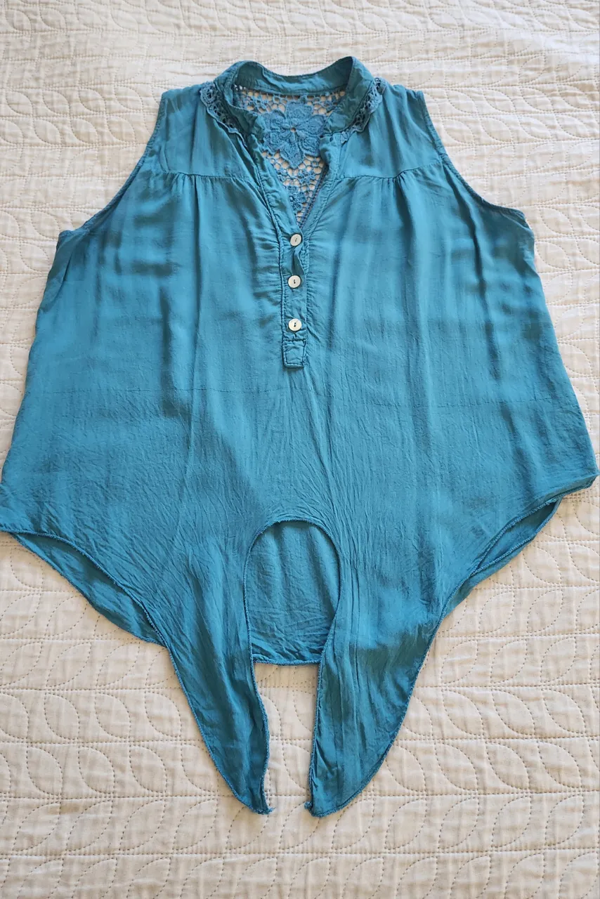 Musculosa azul con cuello redondo y detalles de encaje en la espalda. Posee botones en la parte delantera y un nudo en la parte inferior.