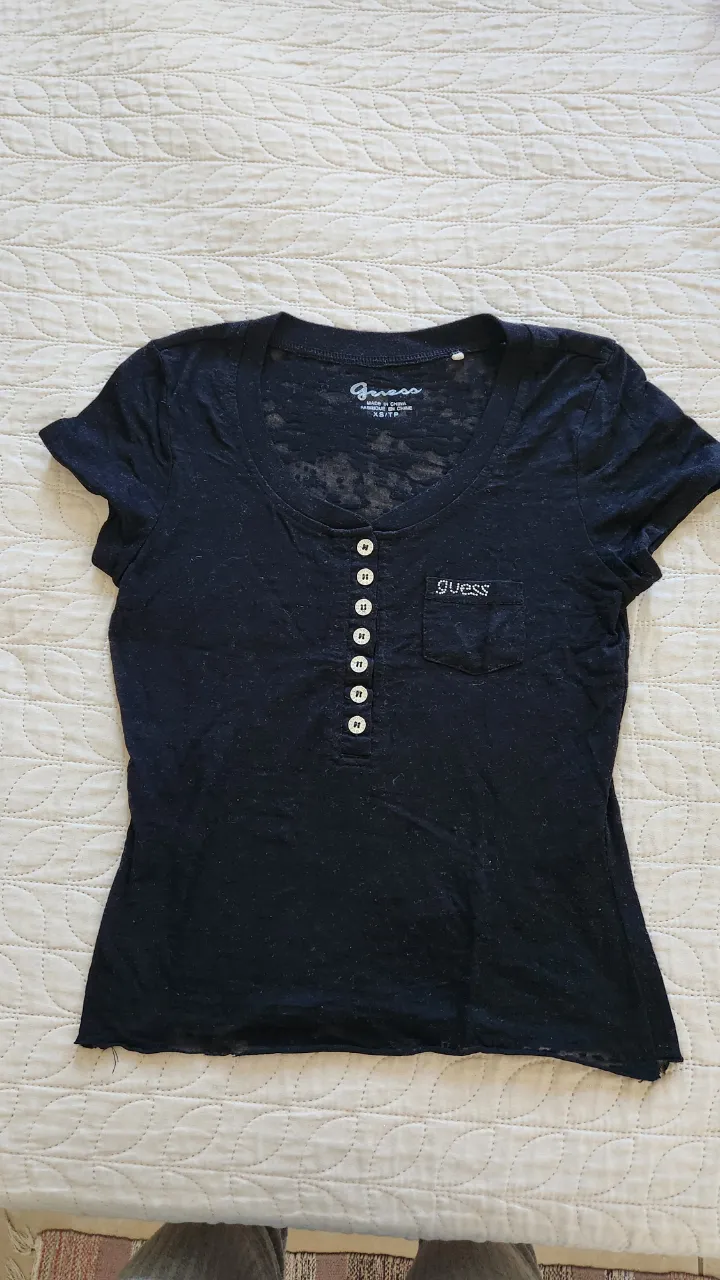 Remera negra de manga corta con cuello redondo y botones al frente. Posee un bolsillo en el pecho.