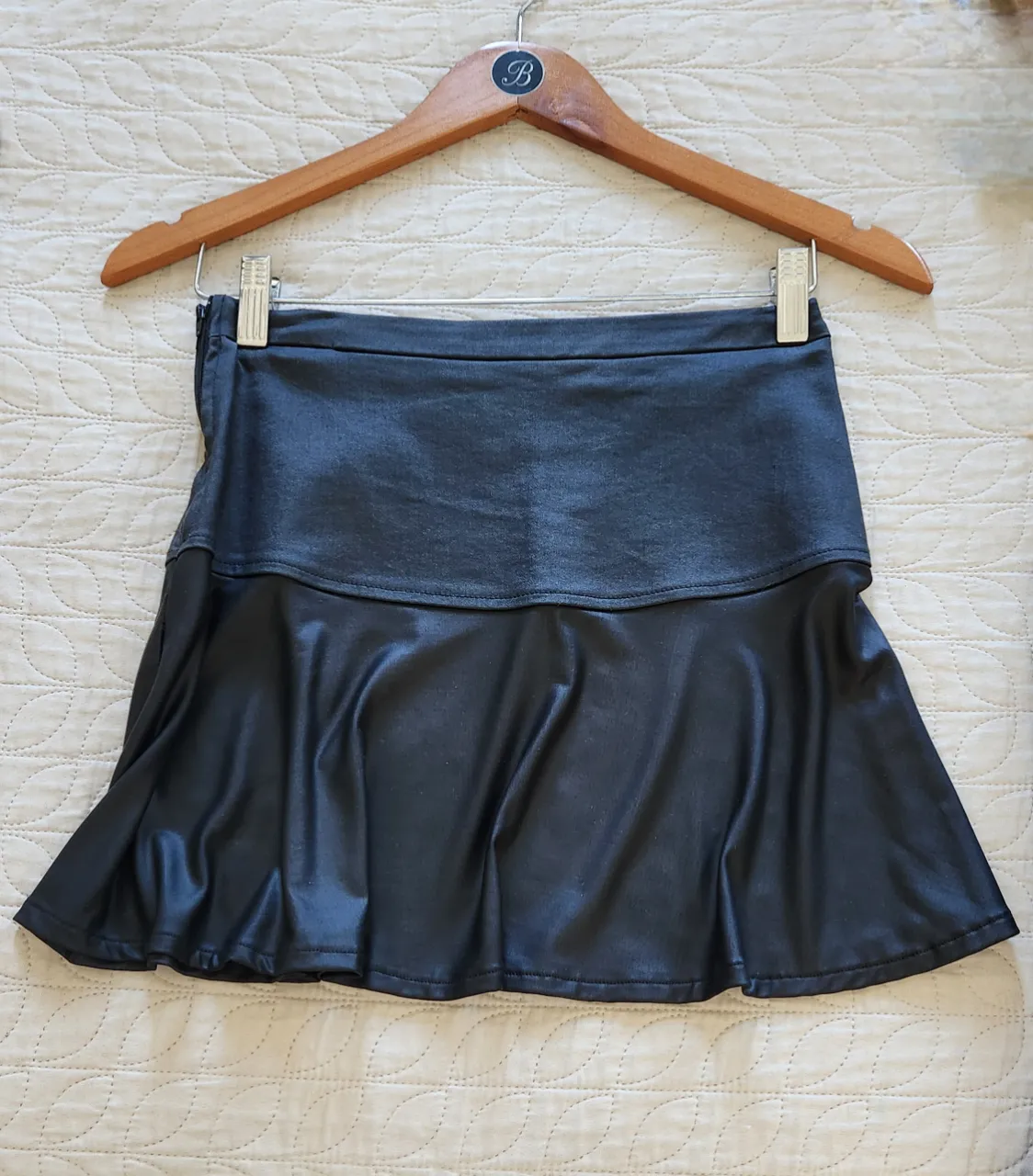 Minifalda corta negra con detalle de tela símil cuero en la parte superior y falda con movimiento. Cierre lateral.