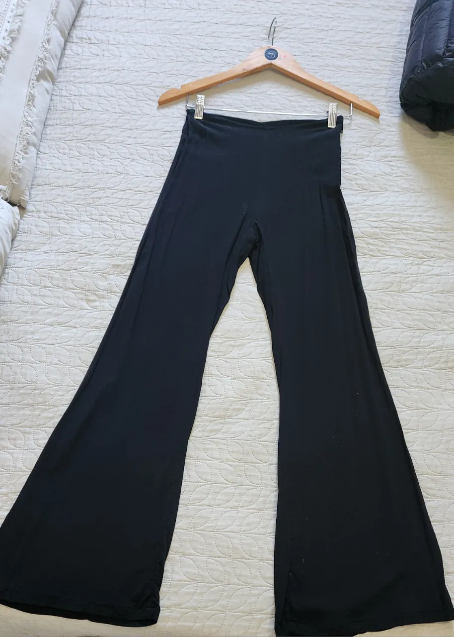 Pantalón negro de tela elastizada, con corte ancho en las botamangas. y cierre al costado.