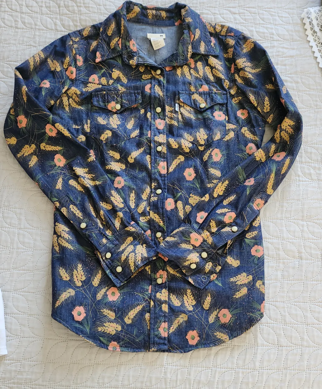 Camisa de jean azul con estampa de espigas y flores en tonos naranja y amarillo. Posee dos bolsillos en el frente con botones a presión. Levi's original.